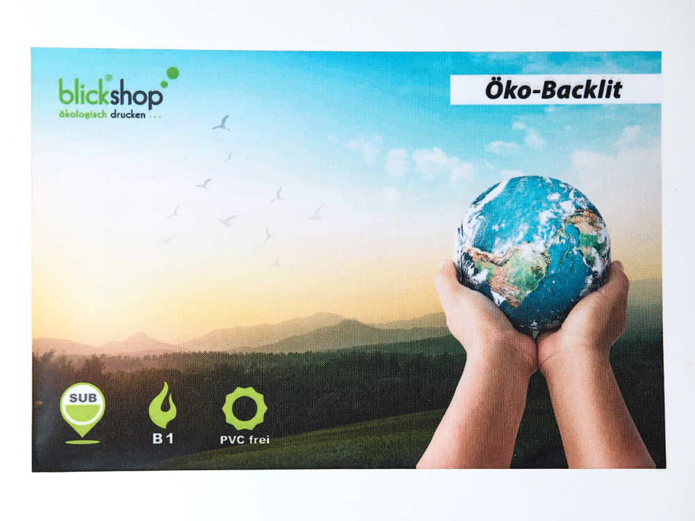 Das bedruckte Materialmuster aus Öko-Backlit zeigt ein Naturmotiv und zwei Hände halten eine Erdkugel. Der Stoff ist lösemittelfrei bedruckt und enthält kein PVC.